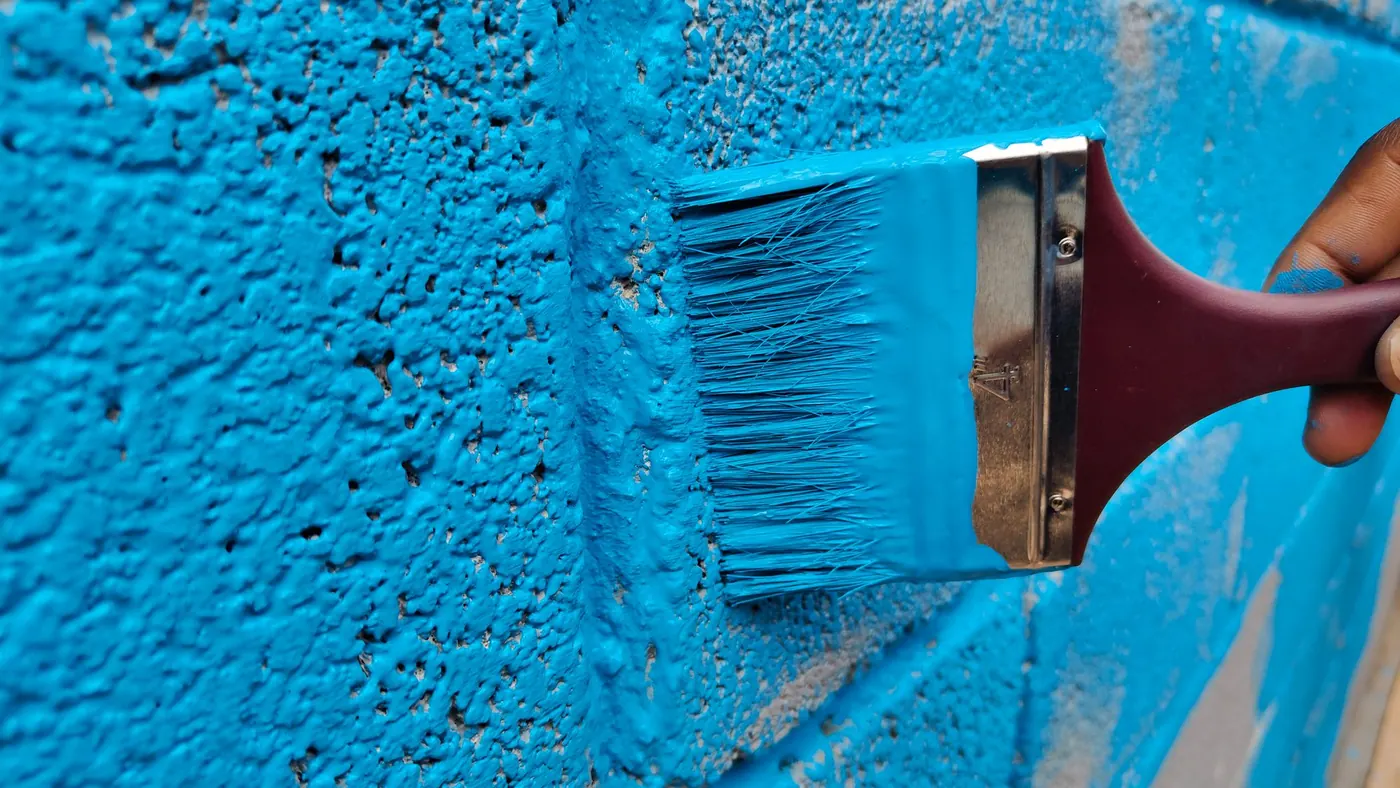A wide brush pushing thick paint into the texture of a brick wall