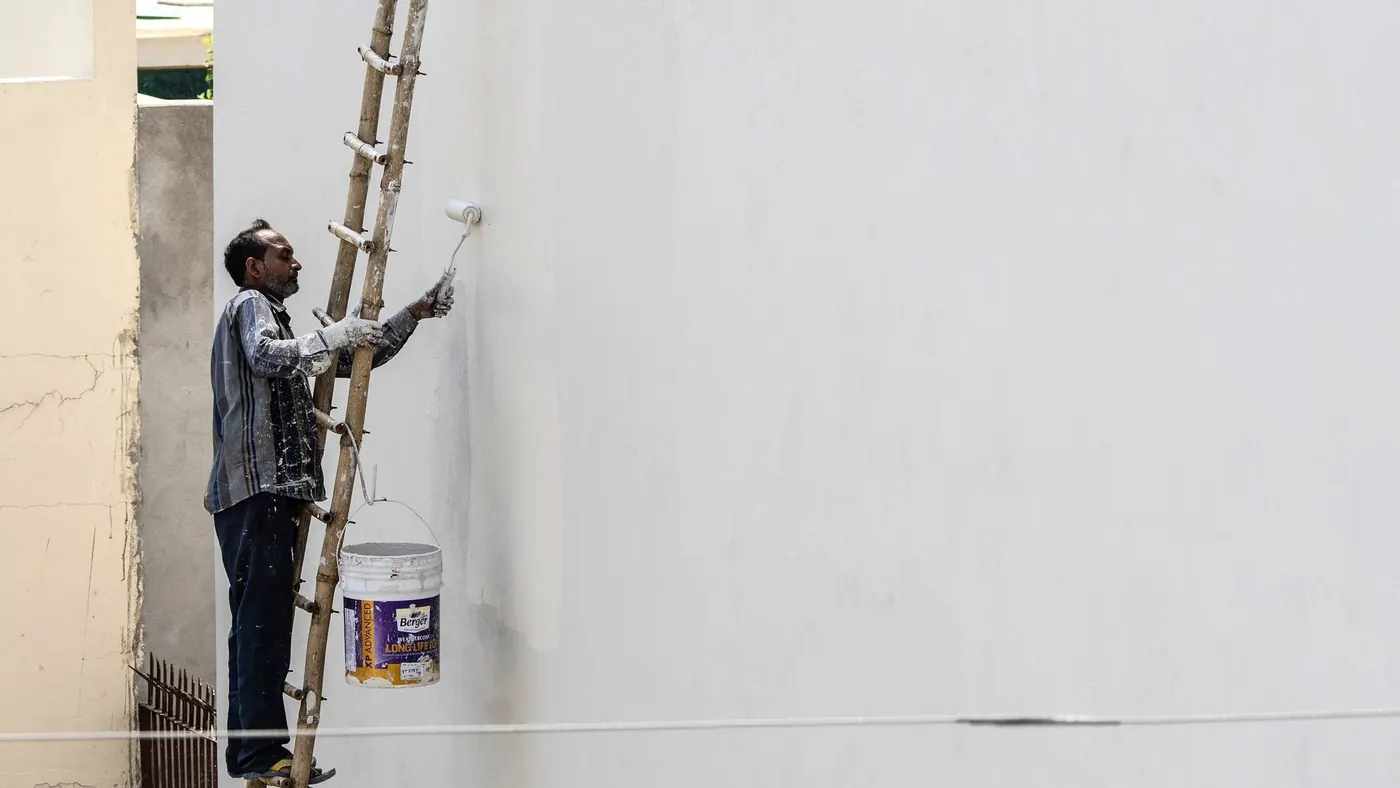 Decorator on a ladder rolling masonry paint onto a rendered wall