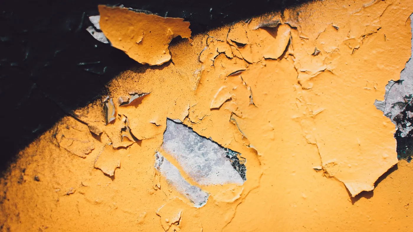 Thick exterior paint peeling away in sheets from a wall