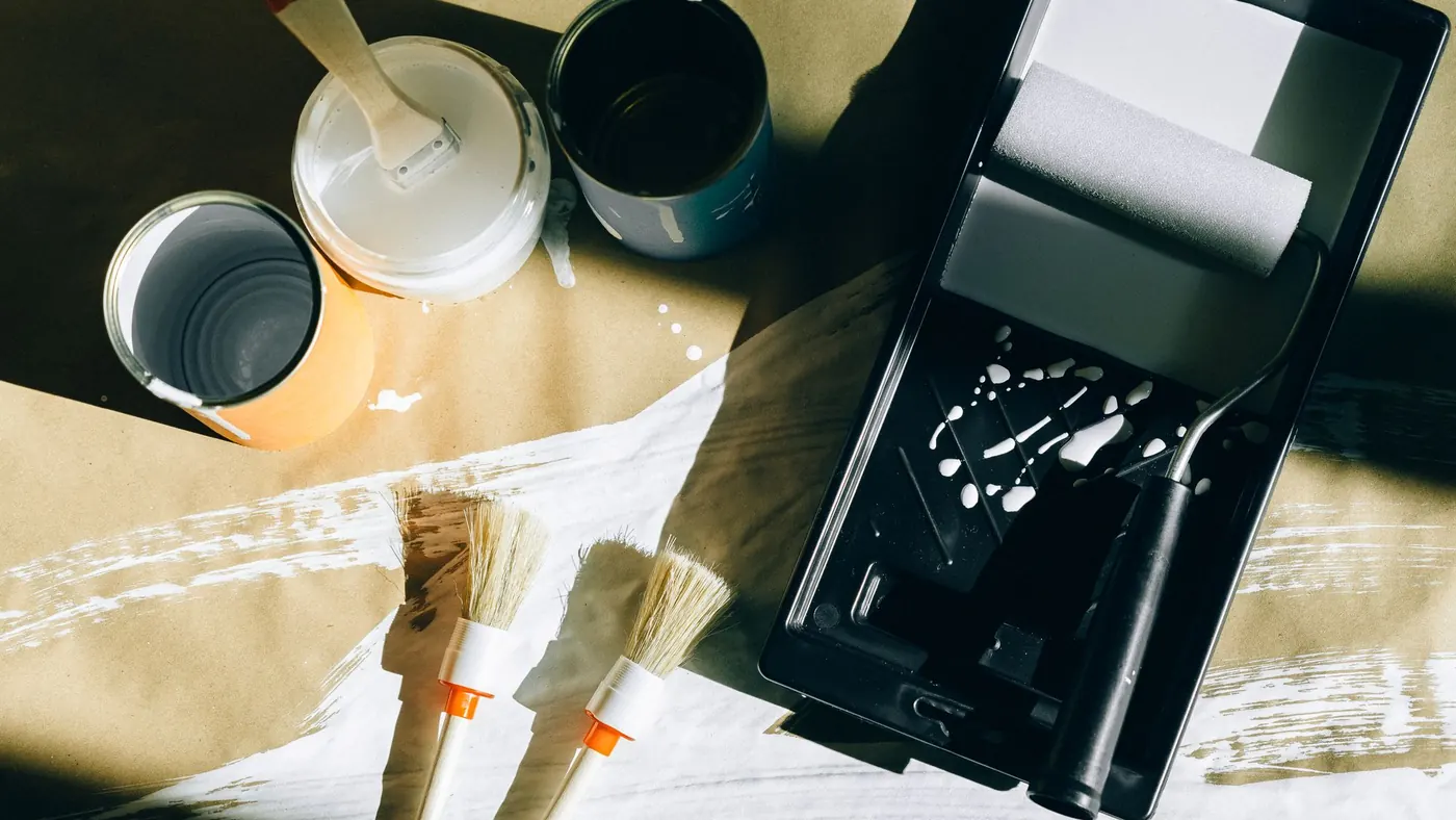 Paint tins, brushes and a roller tray laid out on protective paper