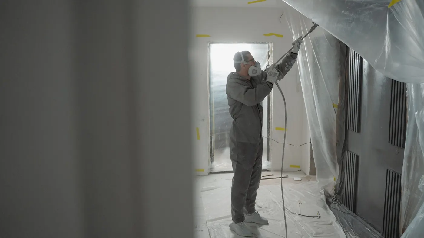 Sprayer working inside a room sheeted in plastic from floor to ceiling