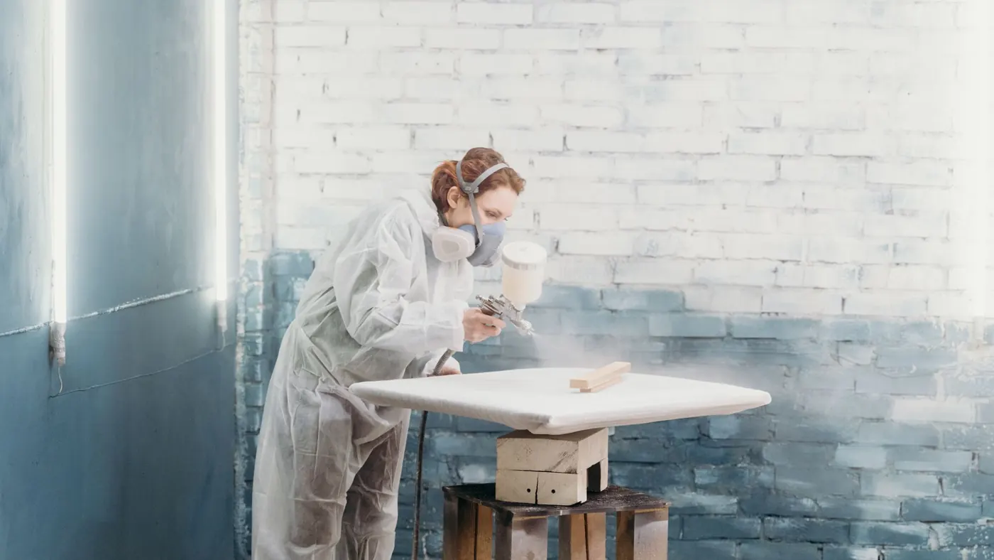 Sprayer in protective gear coating a panel laid flat in a workshop