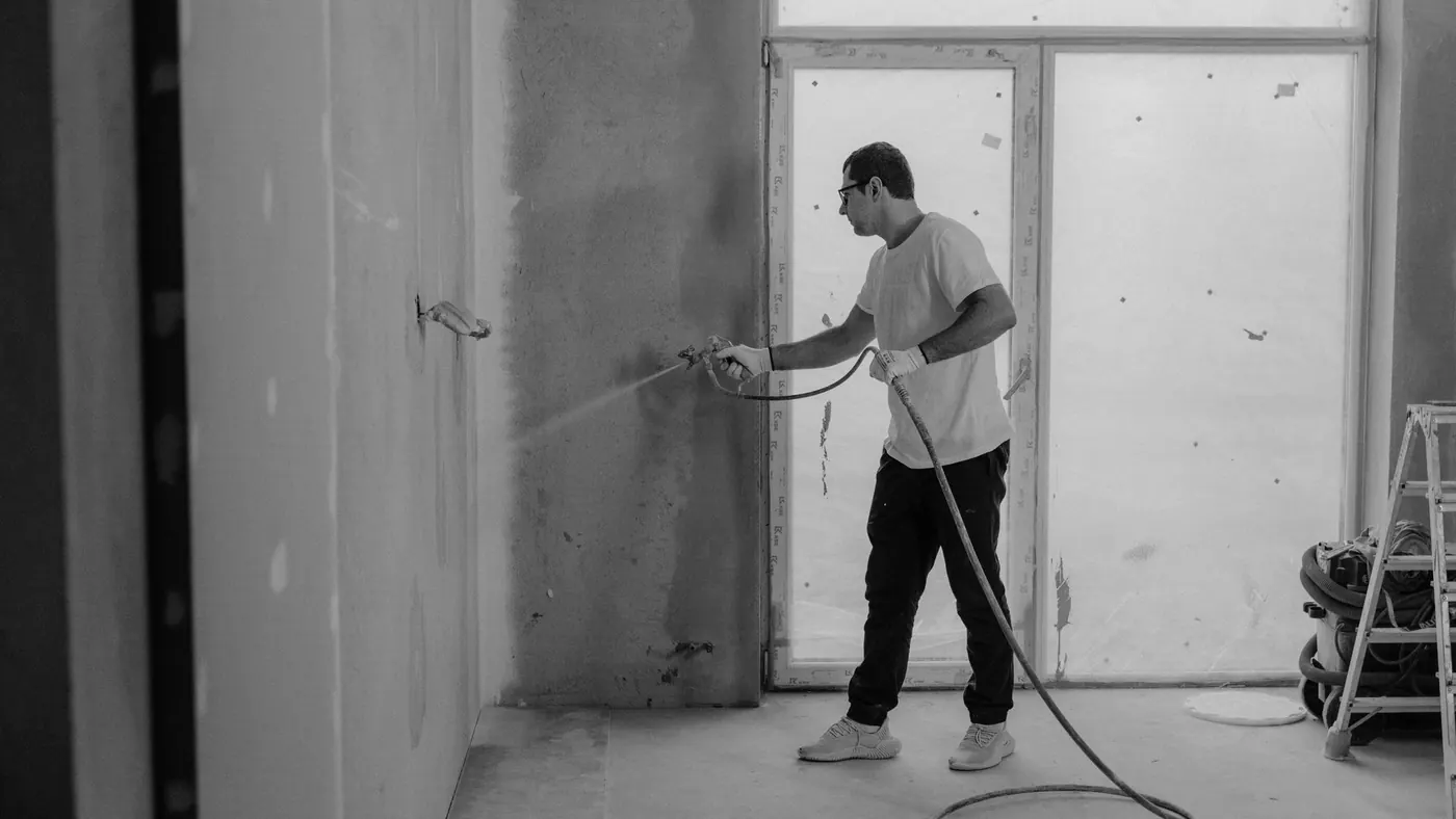 Painter spraying a wall with an airless unit in a bare room