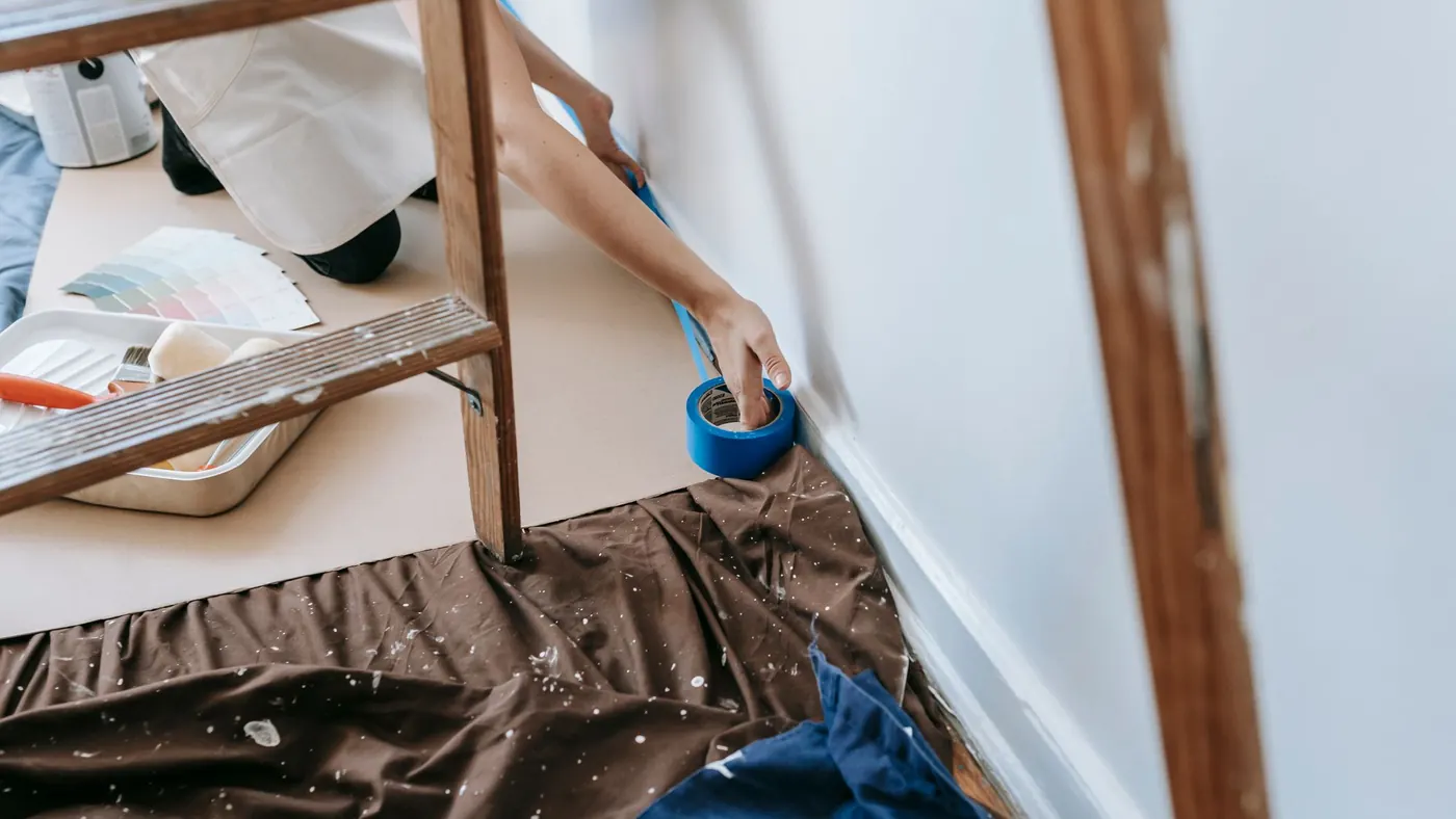 Hands running masking tape along a wall edge before spraying