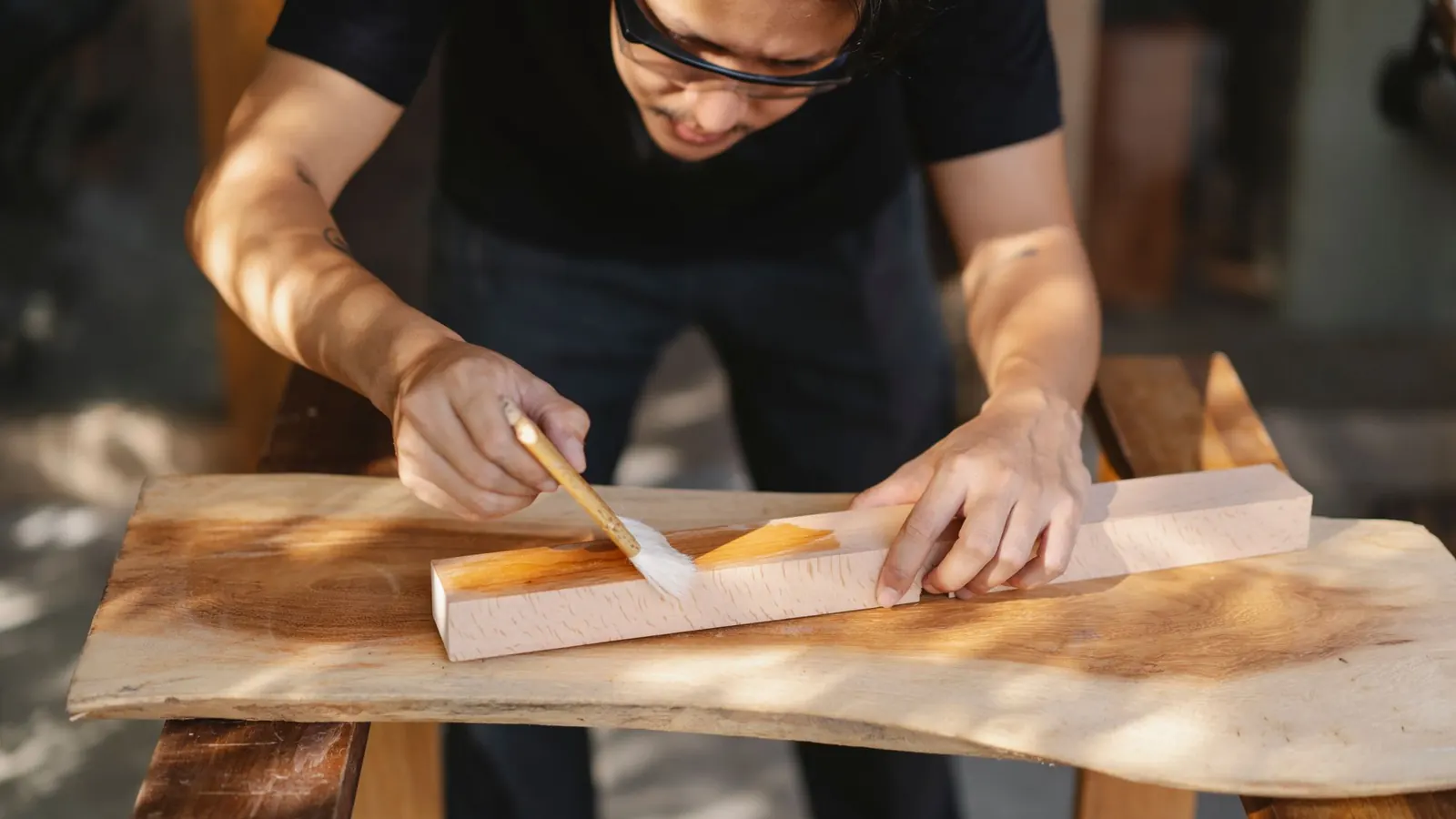 Craftsman brushing a clear finish along the grain of a timber board