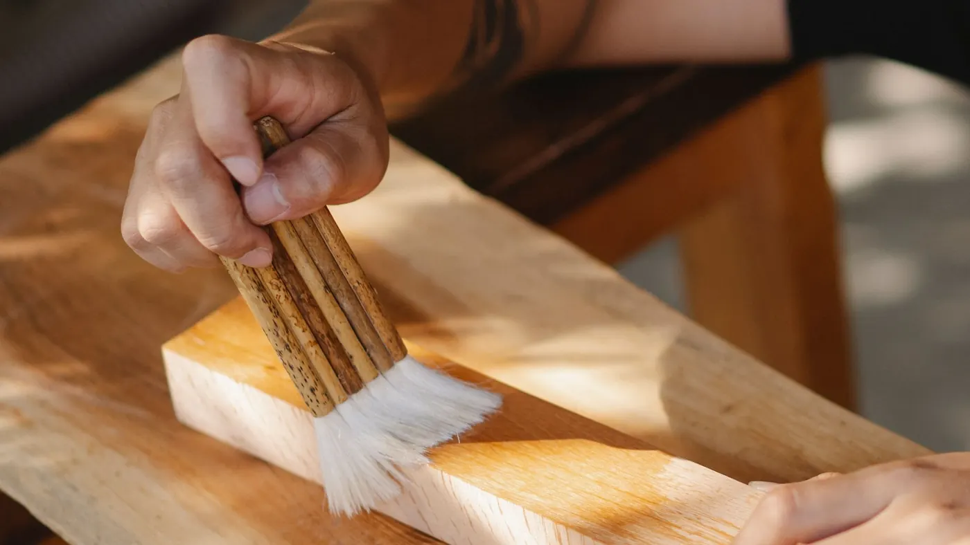 A brush drawing a clear coat across a plank, showing the grain through it
