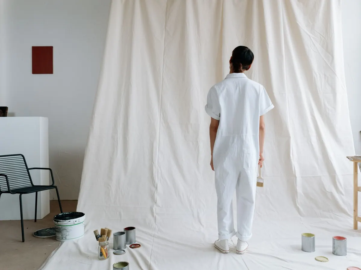 Decorator in white overalls standing in a sheeted room with paint tins