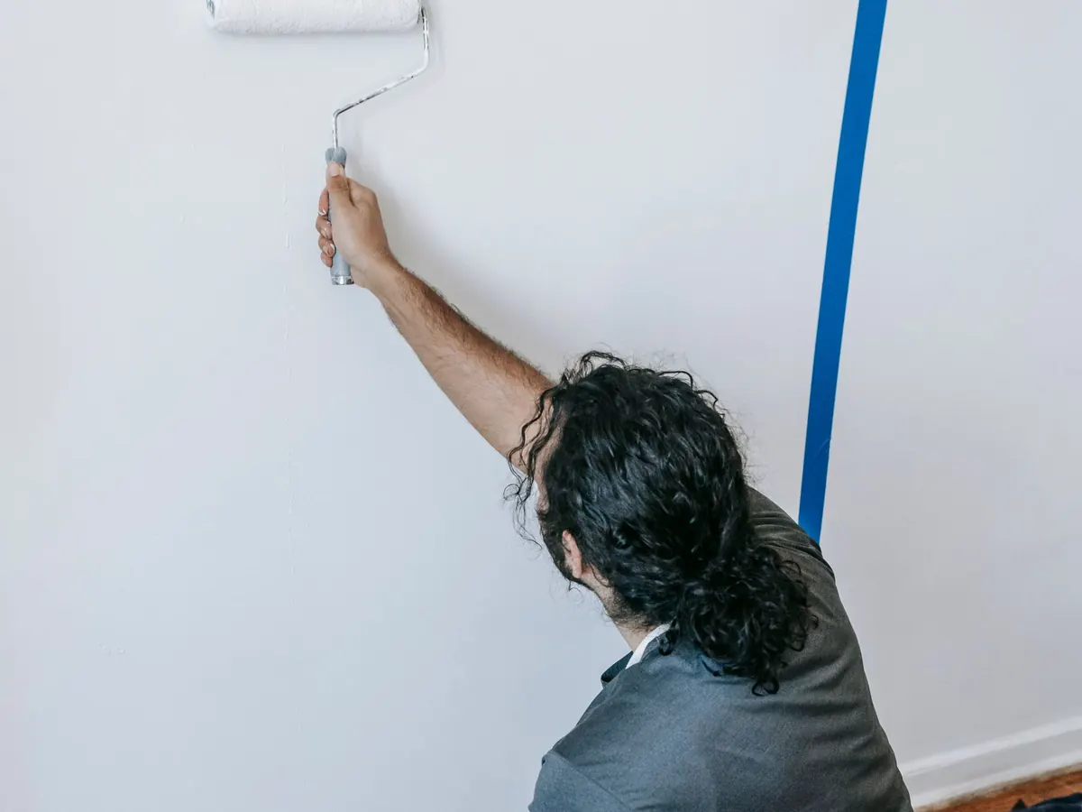 Painter kneeling to roll the lower wall beside masked skirting