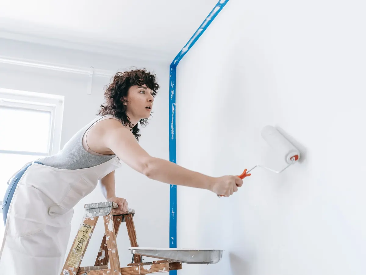 Painter on a ladder working a roller into the top corner of a wall