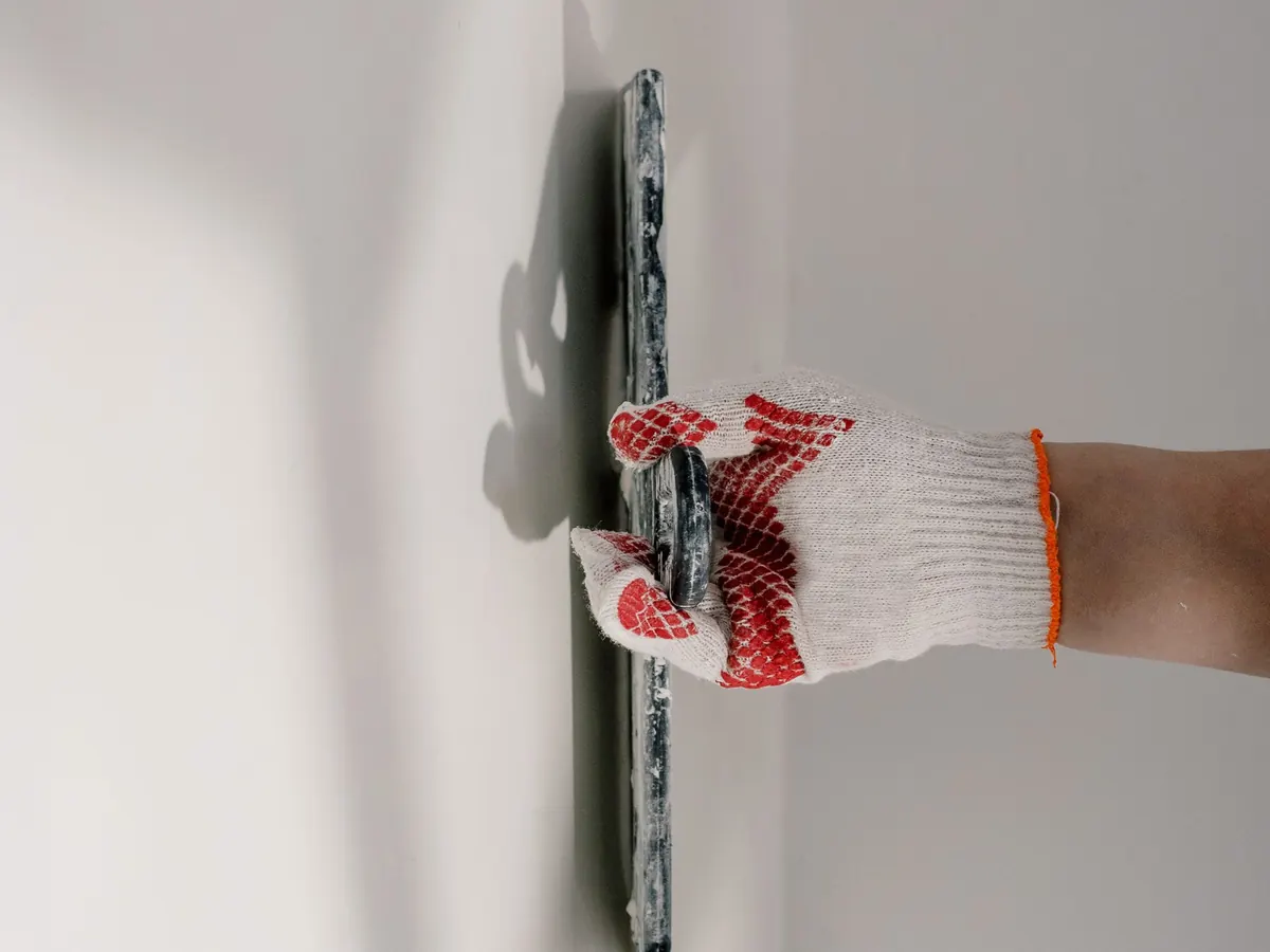 Gloved hand smoothing a fresh skim coat with a trowel