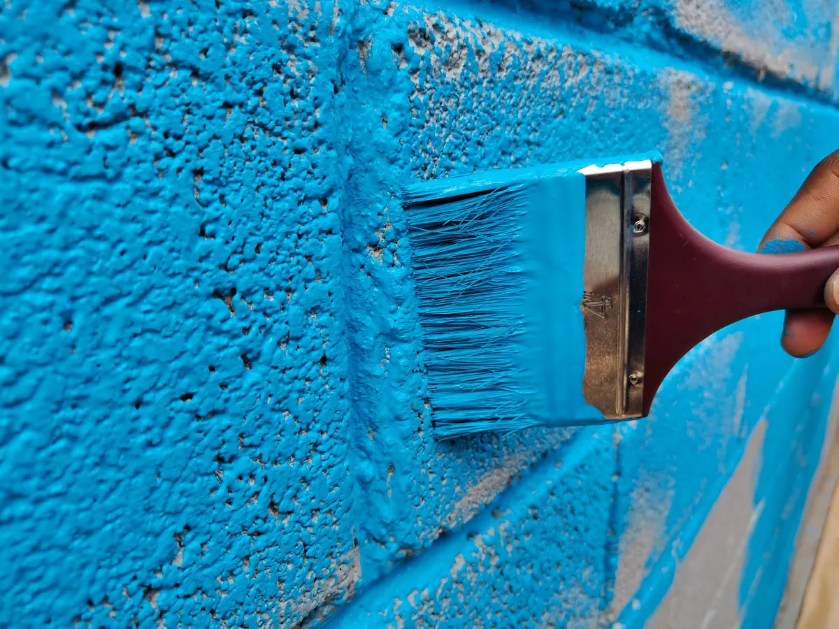 A wide brush working masonry paint into the texture of a brick wall