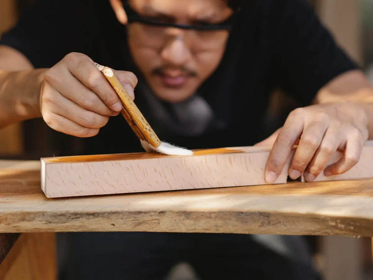Craftsman brushing clear varnish along a timber board
