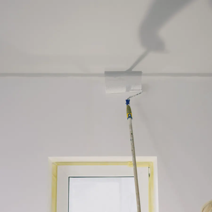 Painter rolling a fresh white ceiling with a long-handled roller
