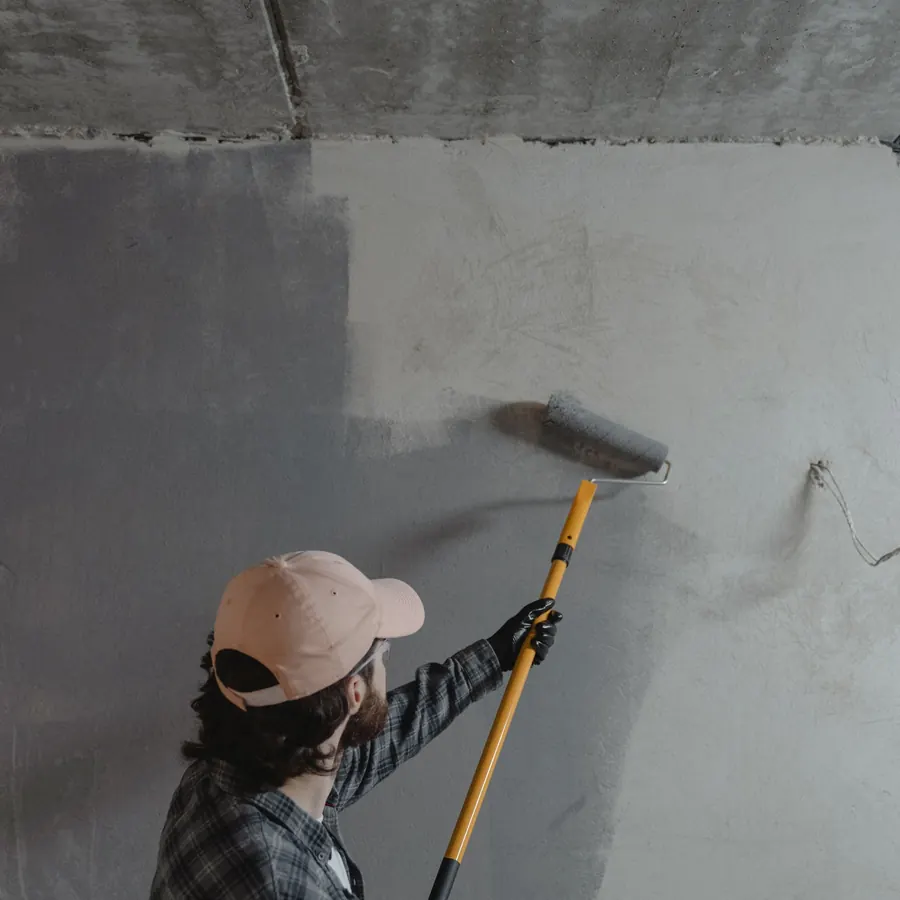 Rolling a mid grey onto a wall in a stripped room