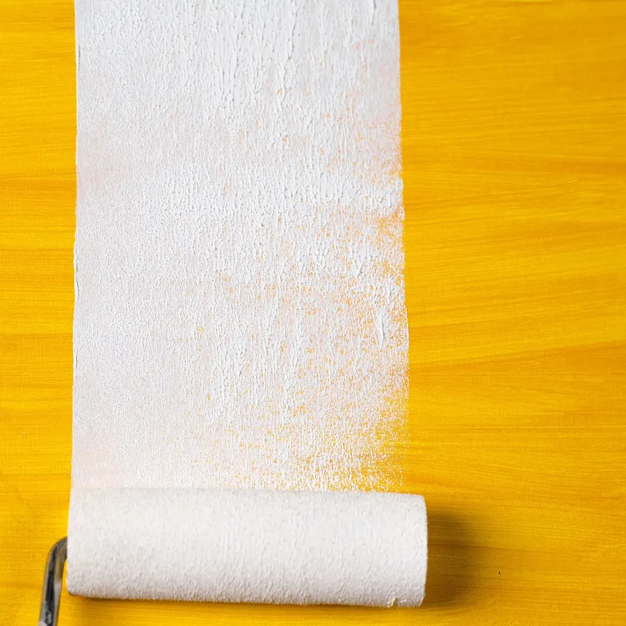 A roller sleeve loaded with white paint over an ochre wall