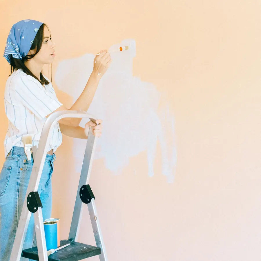 Painter on a stepladder brushing a warm peach colour onto a wall