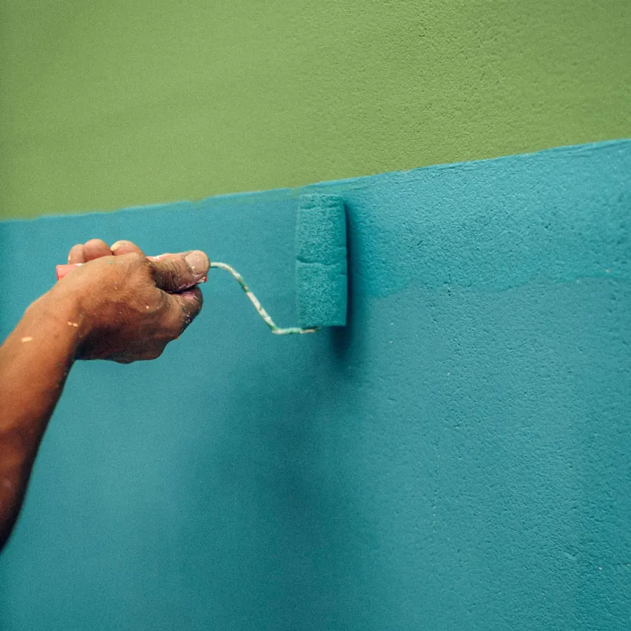 A roller laying a deep teal colour over a lighter first coat