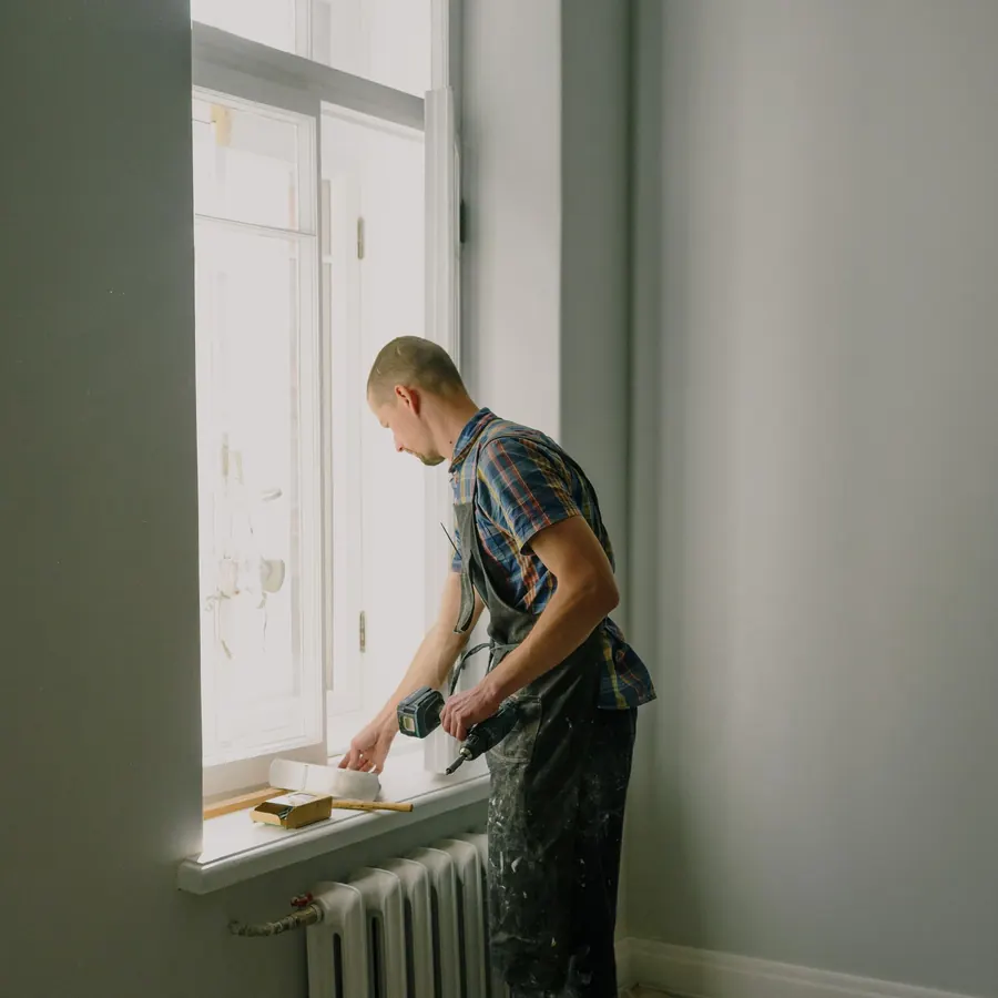 Decorator preparing a window reveal and radiator wall