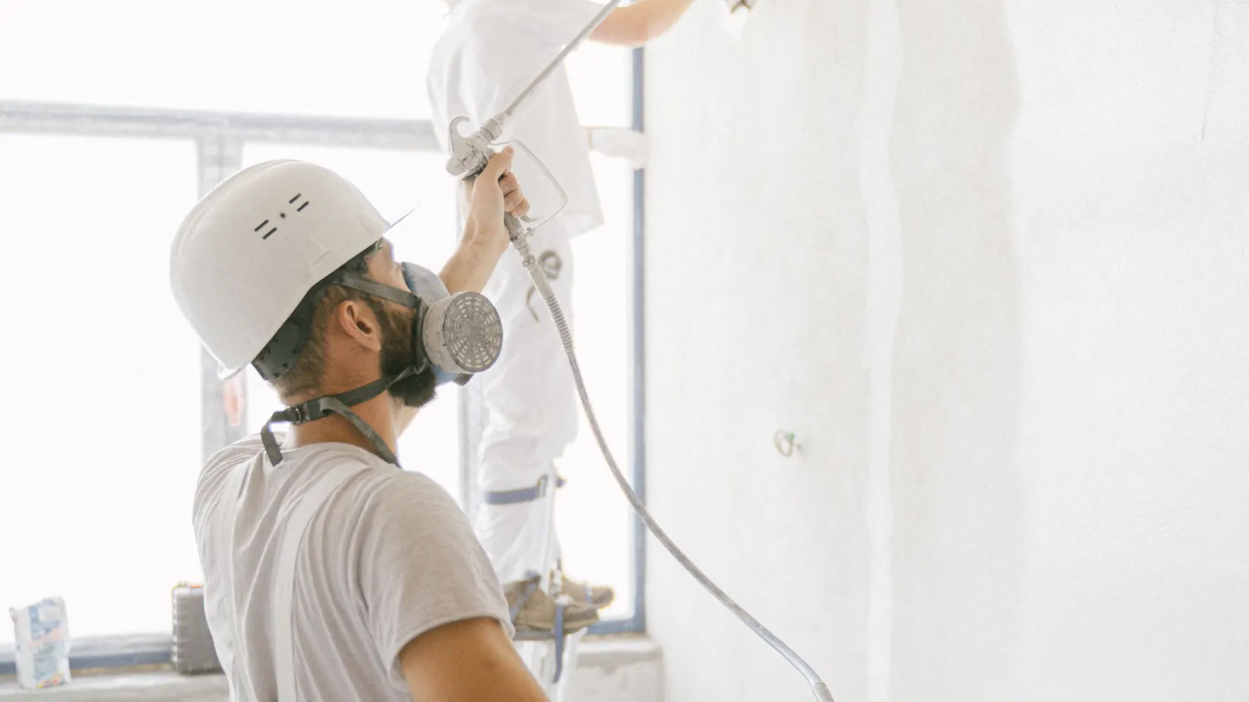 Two decorators in whites painting the walls of an empty commercial unit