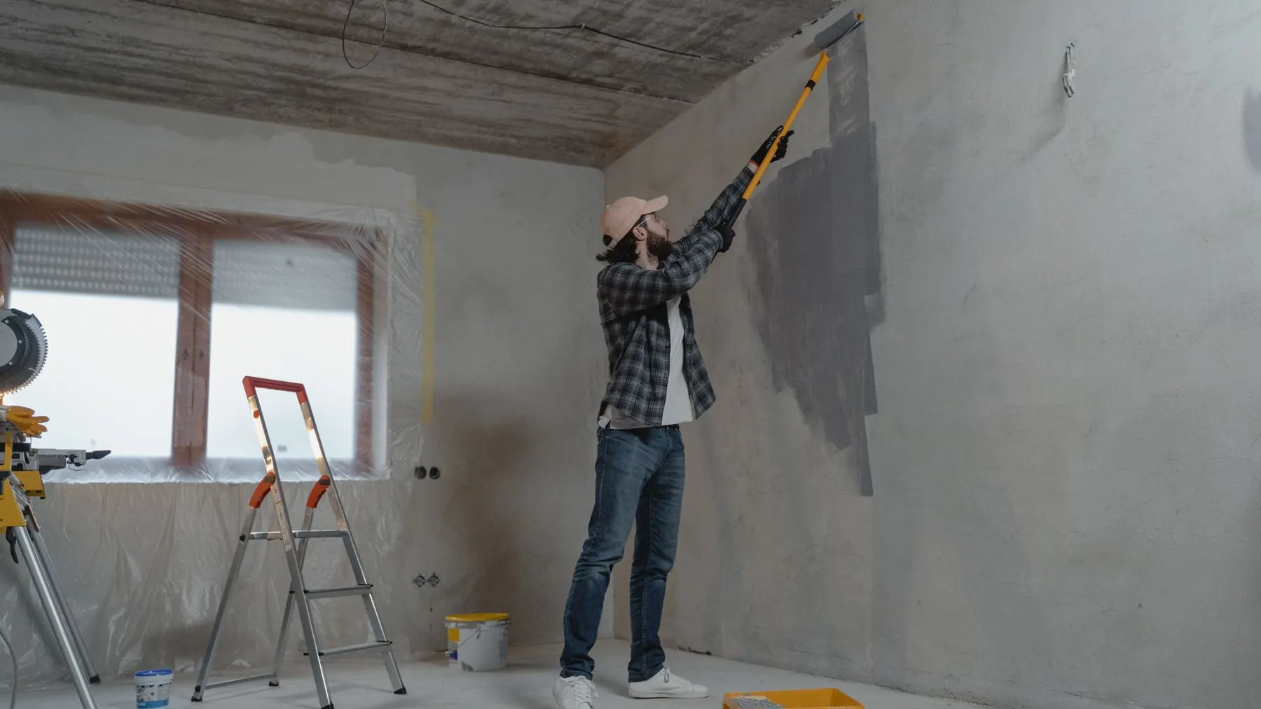 Decorator rolling a fresh coat onto a wall in a sheeted London room